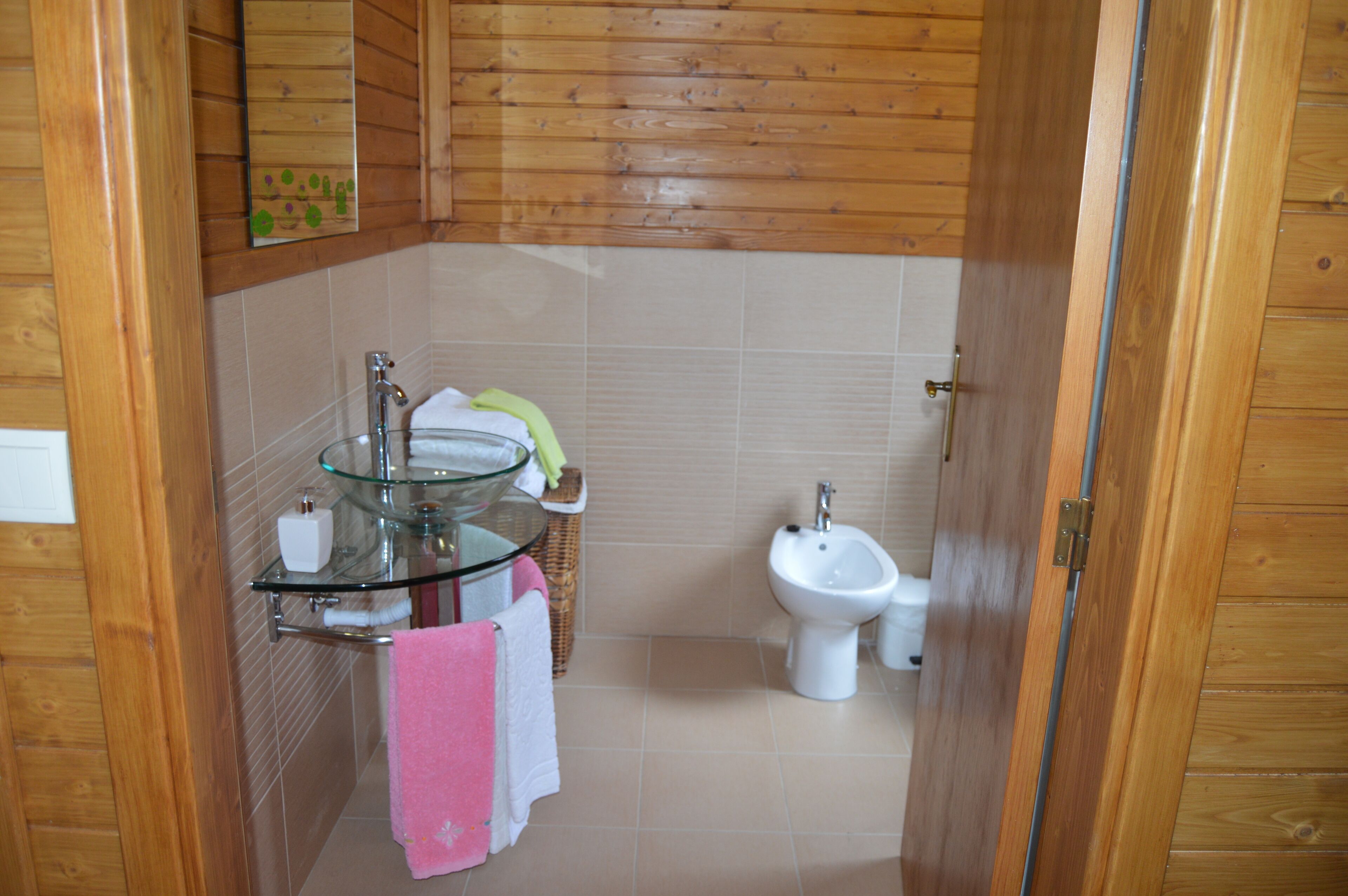 A small bathroom with a glass sink, a bidet, and wooden walls.
