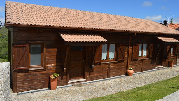 A wooden cabin with a tiled roof, large windows, and potted plants. - Mountain Homes Gralheira - Mountain House (Cinfães)
