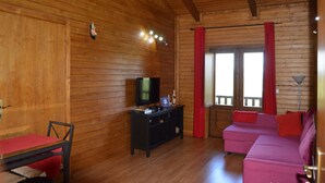 A wooden-paneled room with a television on a black stand, a red sofa, and a red curtain. - Mountain Homes Gralheira - Mountain House (Cinfães)