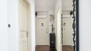 Ein Flur mit weißen Wänden und Holzdielen, der zu einer Tür führt, über der eine Klimaanlage angebracht ist.
