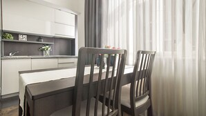 Eine moderne Küche mit weißen Schränken, einem Esstisch mit zwei Stühlen und einem Fenster mit transparenten Vorhängen.