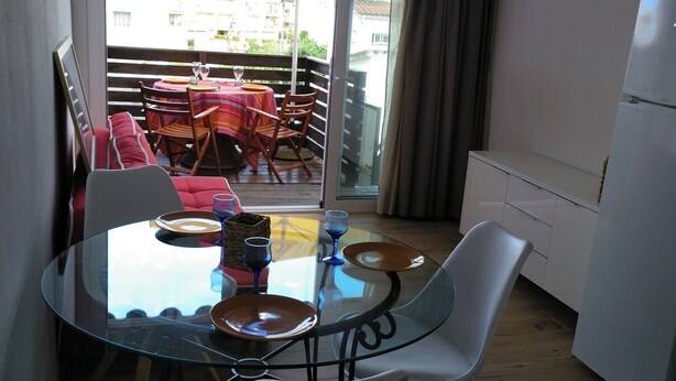 Un coin repas avec une table en verre, des chaises blanches et une vue sur un balcon aménagé avec des sièges d’extérieur.