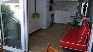 Une cuisine compacte avec des meubles blancs, un four à micro-ondes et un évier. On y trouve également un coin repas avec un canapé rouge et une chaise en bois.