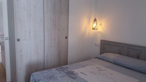 Une chambre à coucher comprenant un lit, une table de chevet, une lampe fixée au mur et une armoire en bois.