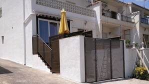 Un bâtiment à deux étages, à la façade blanche, doté d’une entrée fermée par un portail et surmonté d’un parasol jaune.