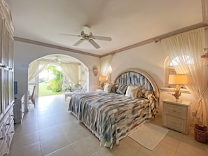 A bedroom with a bed, a nightstand, a ceiling fan, and a view of the garden.