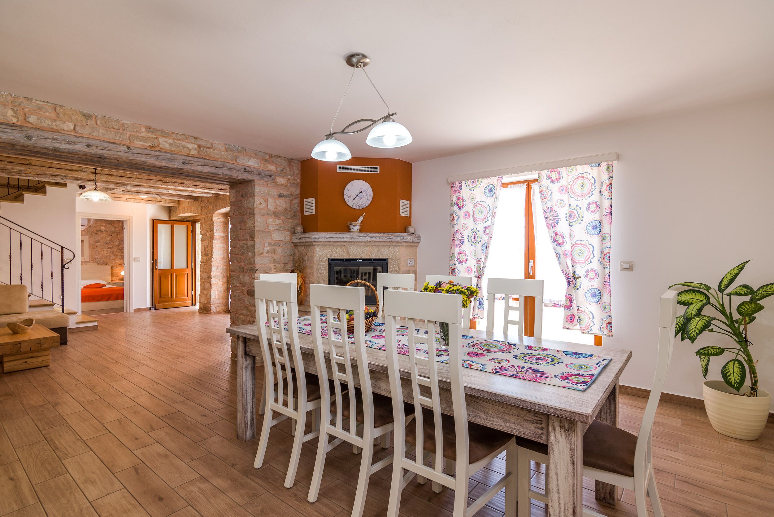 Un coin repas avec une table en bois, des chaises blanches, une cheminée et une horloge au mur.