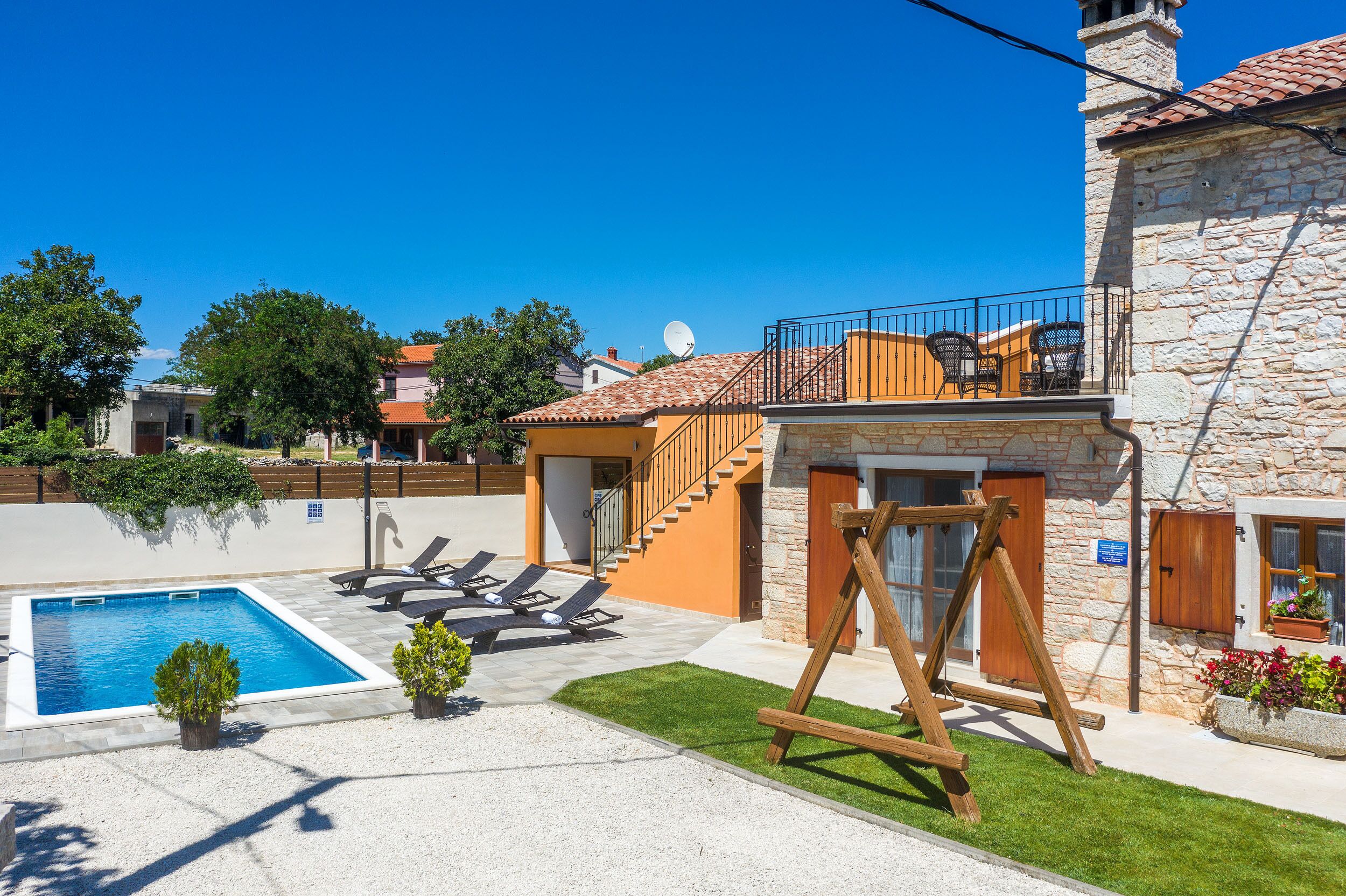 A residential property with a swimming pool, outdoor seating, and a stone building.