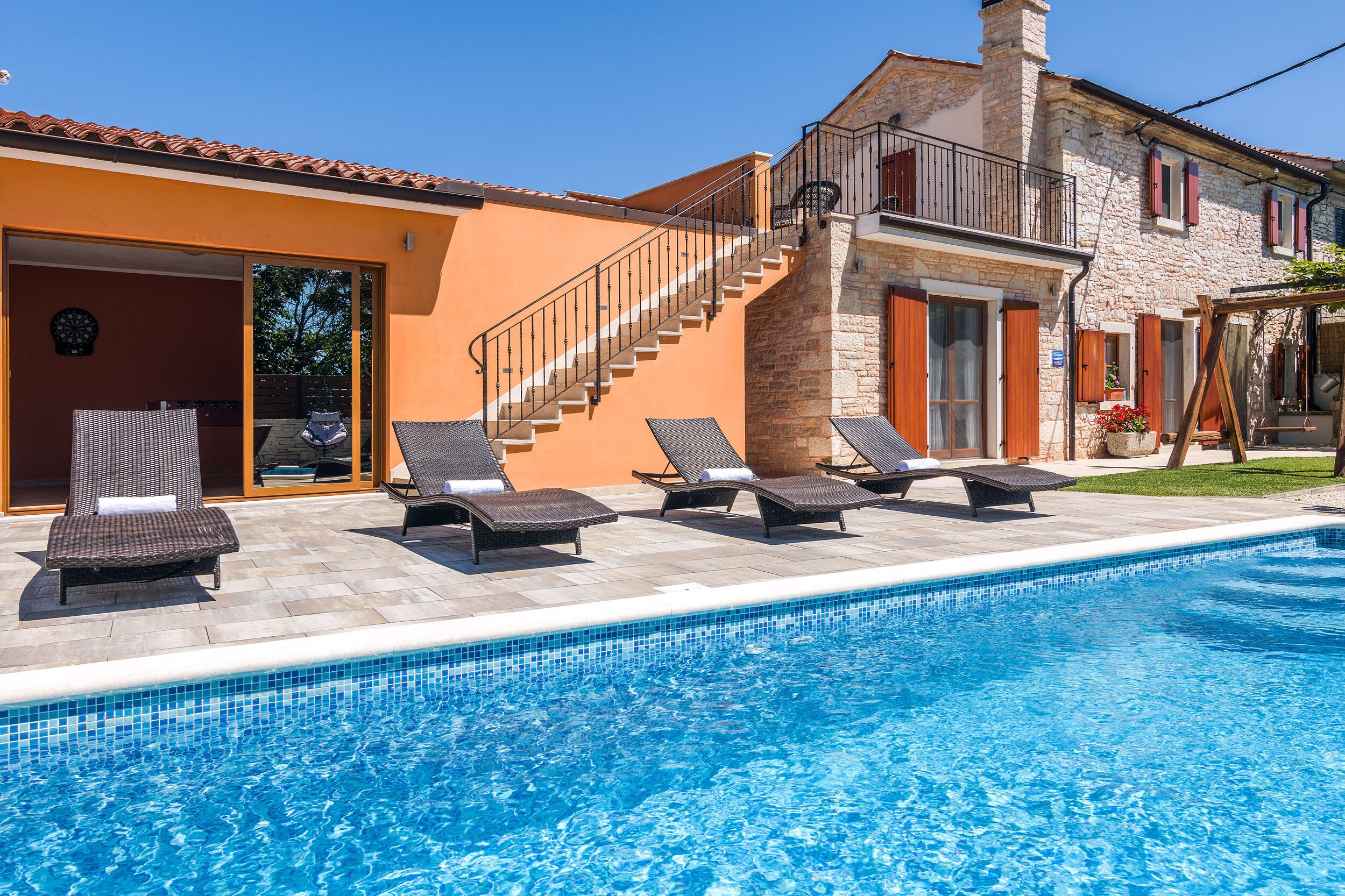 A swimming pool with lounge chairs, a staircase, and a stone building with a tiled roof.