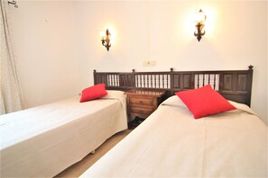 A double room with two single beds, each with a red pillow, a wooden nightstand, and a wall-mounted light fixture.