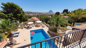 Ein Pool auf dem Dach mit Liegestühlen und Sonnenschirmen, umgeben von Palmen und Blick auf Stadt und Berge.