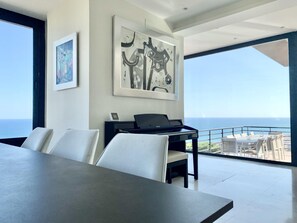 Enjoy a panoramic ocean view from the comfort of this stylish room, featuring a large window, a dark-toned table, and a balcony with a railing.
