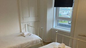 Two single beds with white linens and a window with a view of a building and street. - Elderpark Apartment 4 (Glasgow)