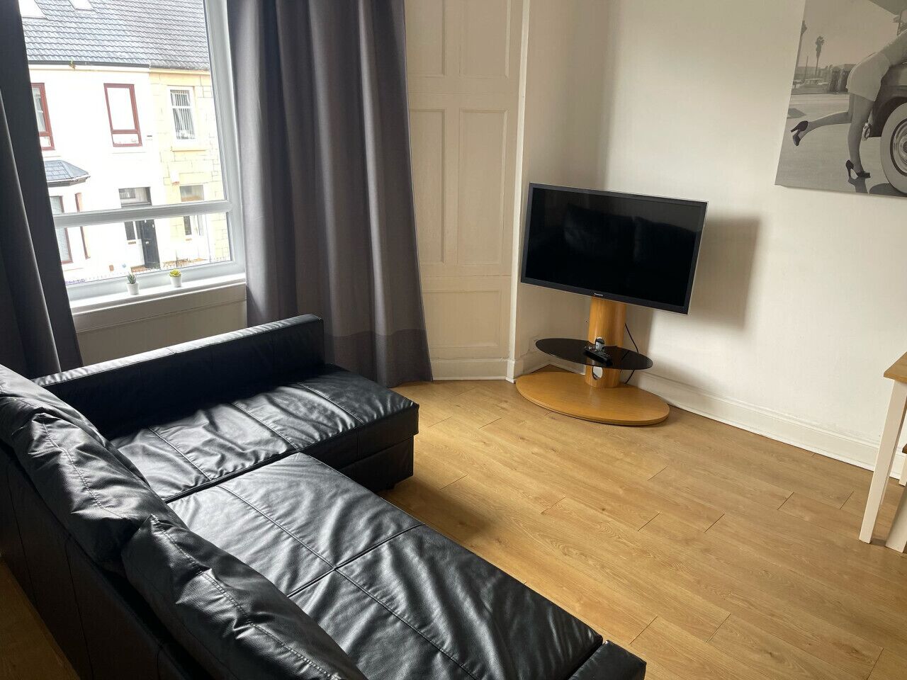 A modern living room with a black leather sofa, a flat-screen TV on a wooden stand, and a window with curtains.