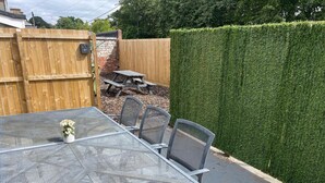 A metal table with chairs, a small potted plant, and a wooden fence in the background. - Elderpark Apartment 4 (Glasgow)