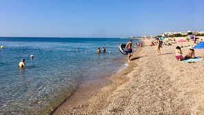 Una spiaggia con acqua cristallina, un litorale di ciottoli e persone che prendono il sole e nuotano.