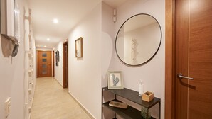 Un corridoio con una porta in legno, uno specchio tondo, uno scaffale con una cornice e un porta scarpe.