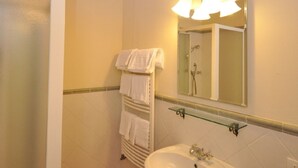 A bathroom with a white sink, a glass shelf, a towel rack with multiple towels, a mirror with a light, and a shower area. - LECCINO ROOM at Agriturismo MUSIGNANO (cerreto guidi)