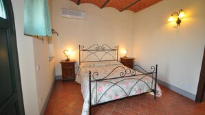 A bedroom with a bed, two bedside tables with lamps, a wall-mounted air conditioner, and a decorative light fixture. - LECCINO ROOM at Agriturismo MUSIGNANO (cerreto guidi)
