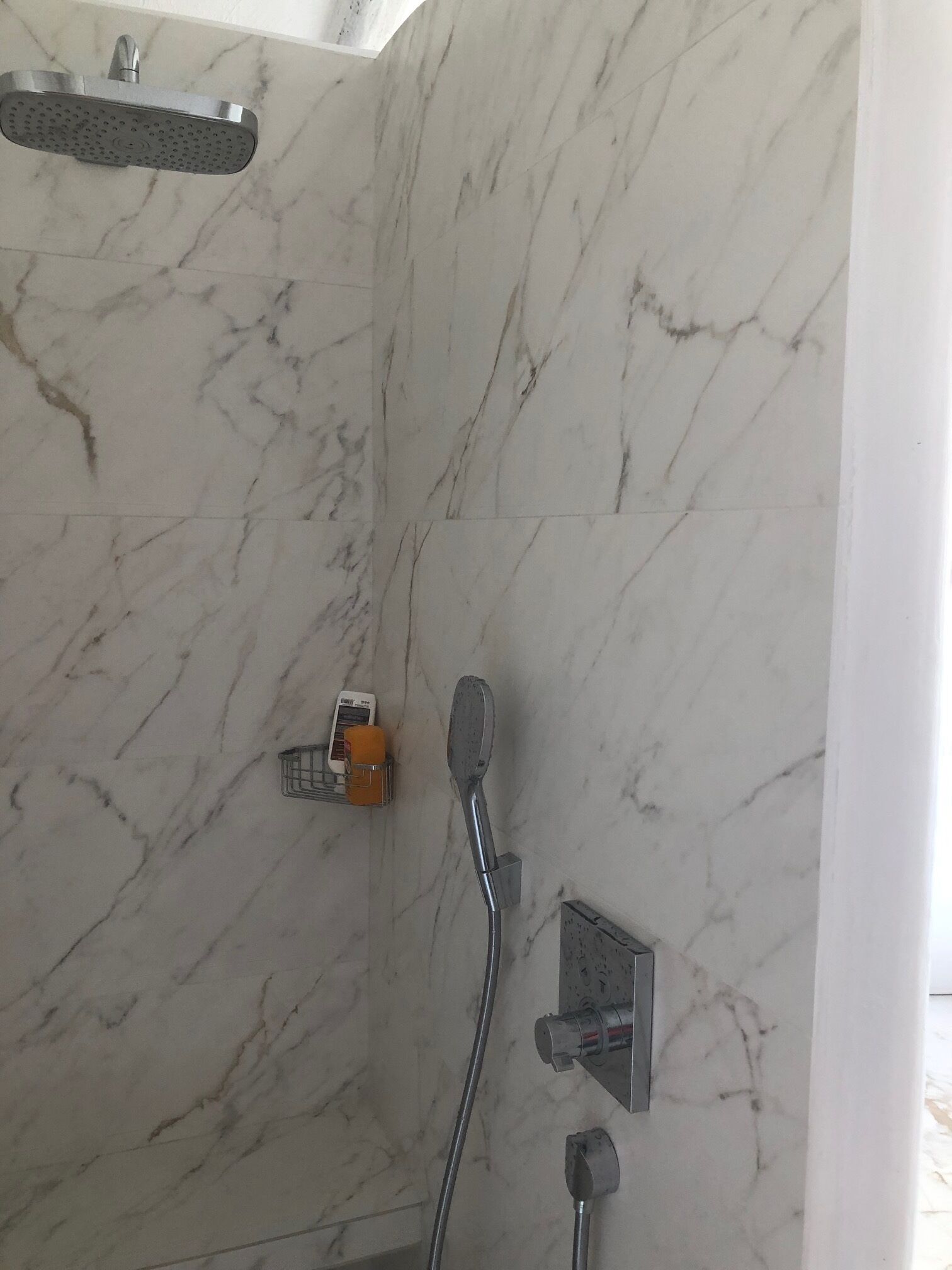 A bathroom with a shower, a handheld showerhead, and a wall-mounted control panel.