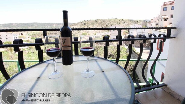 Un balcon avec une table, deux verres à vin et une bouteille de vin.