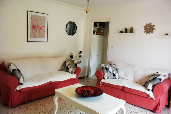 Una sala de estar con dos sofás rojo y blanco, una mesa de centro blanca y un cuadro en la pared.