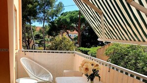 A balcony with a white table, two white chairs, a vase with flowers, and a view of trees and buildings.