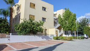 Un edificio moderno de varios pisos con balcones, rodeado de vegetación y un área pavimentada.