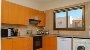 Eine kleine Küche mit Holzausstattung, integriertem Backofen, Geschirrspüler und einem Fenster mit Blick auf umliegende Gebäude.