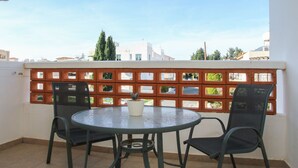 Un balcón con una mesa redonda y dos sillas, una planta en maceta y una valla de madera.