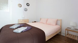 Een slaapkamer met een bed, een houten nachtkastje, een kleine tafel en een raam.