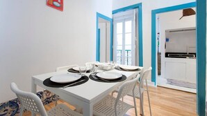 Een eetruimte met een witte tafel voor vier personen, witte stoelen, en een keuken zichtbaar door een open deur.