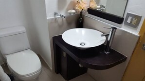 Ein kleines Badezimmer mit Toilette und Waschbecken in Weiß, einer schwarzen Arbeitsplatte und einem Spiegel über dem Waschbecken.