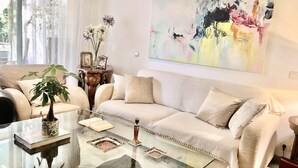 Ett modernt vardagsrum med en beige soffa, ett soffbord i glas och en stor, abstrakt tavla på väggen.