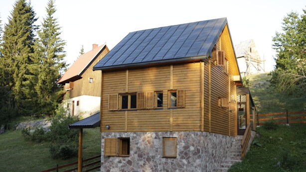 A wooden cabin with a sloped roof, stone foundation, and wooden shutters on the windows.