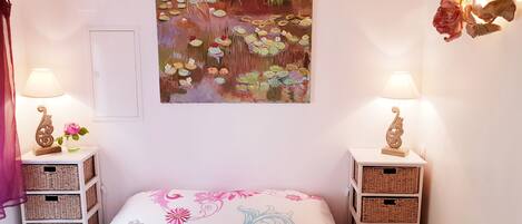 Un dormitorio con una cama, dos mesitas de noche con lámparas, cestas de mimbre, un cuadro y una puerta.
