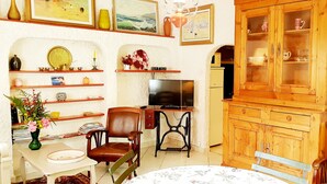A cozy living room with a television, wooden cabinets, and a dining area with chairs and a table. - ARTIST'S HOME, 5 MINUTES FROM THE SEA, VERY QUIET, TUCKED AWAY IN A LUSH GREEN SETTING. (Trégastel)