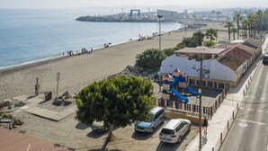 Vista sulla spiaggia con un'area giochi, auto parcheggiate e una visuale libera sul mare.