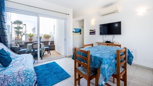 Une chambre moderne équipée d’un lit, d’une table à manger avec des chaises, d’un téléviseur et d’un balcon agrémenté de plantes.