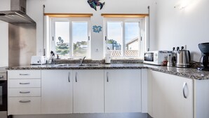 Une cuisine moderne avec des armoires blanches, un comptoir en granit, une hotte de cuisinière en acier inoxydable, un four à micro-ondes, une machine à café et un évier.