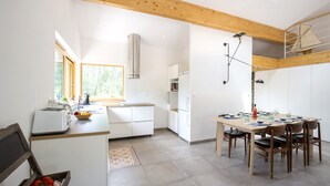 Una cocina moderna con armarios blancos, techo de madera y comedor con mesa lista para cuatro.