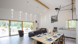 Un comedor moderno con una mesa de madera dispuesta para cuatro personas, un sofá y un amplio ventanal con vistas al exterior.