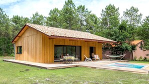 Una cabaña de madera con techo de tejas, ventanas amplias y un patio con mobiliario exterior.