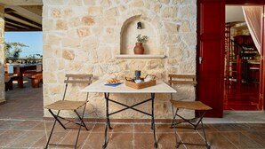 A stone wall with a shelf holding a vase and a candle, a table with chairs, and a red door. - Lilas Luxury Villa, is a stone manor with its own private pool . (Zakynthos)