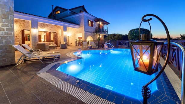 A swimming pool with lounge chairs and a lantern, surrounded by stone walls and a house with a balcony. - Lilas Luxury Villa, is a stone manor with its own private pool . (Zakynthos)