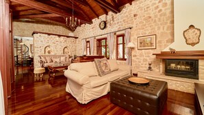 A cozy living room with a stone wall, wooden beams, a fireplace, and a sofa. - Lilas Luxury Villa, is a stone manor with its own private pool . (Zakynthos)