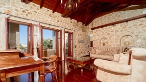 A spacious living area with a stone wall, wooden furniture, and a fireplace. - Lilas Luxury Villa, is a stone manor with its own private pool . (Zakynthos)