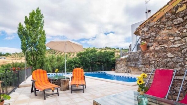 Terrassa exterior amb dues cadires de ratlles taronja, una taula, una piscina i una paret de pedra.