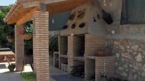 Zona de terrassa a l'aire lliure amb una estructura de barbacoa de maó, taules de fusta i un mur de pedra.