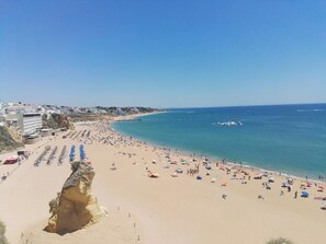 Ein Strand mit einer Felsformation, einem weiten Sandbereich und einem klaren, blauen Meer.